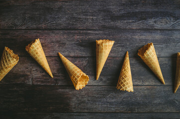 Waffle cones are neatly aligned on a rustic wooden surface, showcasing their crispy texture and...