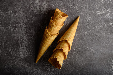 Two waffle cones are positioned on a dark surface, highlighting their crispy texture and inviting...