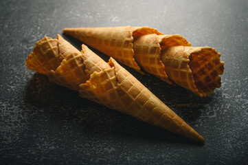 Two waffle cones rest on a dark textured surface, waiting to be filled with delicious ice cream....