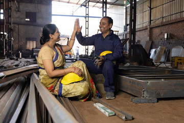 Two indian engineers wearing safety hard hat and vest laughing and talkin at industrial factory, skill india concept.