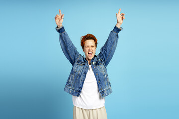 Excited young woman celebrating with arms raised on blue background in studio