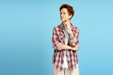 Portrait of trendy young woman in plaid shirt posing in studio, isolated on blue