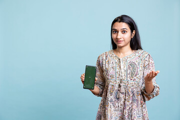 Portrait of indian woman doing marketing ad with green screen device, standing against blue...
