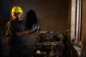 Engineer in protective workwear inspecting lathe at factory