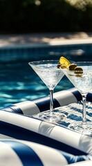Two elegant martini glasses filled with sparkling cocktails and garnished with olives and a lemon twist, resting on a striped float in a tranquil pool setting, capturing relaxation.