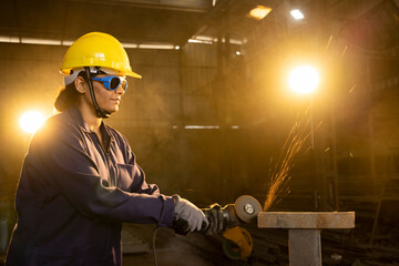Side view portrait of mature female worker cutting metal at industrial plant.