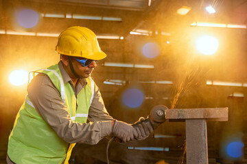 Mechanic using circular saw grinder tool with protective work wear at factory.