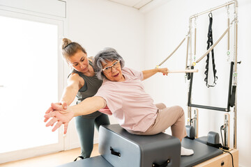 Pilates Instructor Guiding Elderly Woman During Exercise Session in Bright Studio