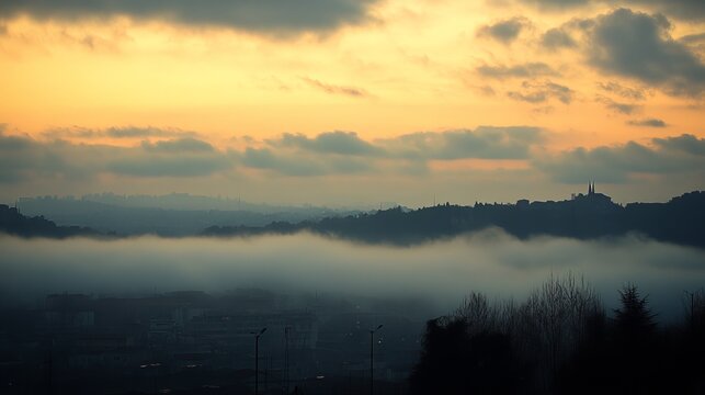 Misty sunset over a cityscape nestled in rolling hills, a blanket of fog obscuring the lower town