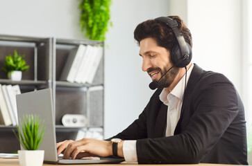 Fototapeta premium Call center operator agent sitting at the desk desk in headset working on laptop, communicating with clients in office for customer service. Technical support and help desk agency concept.