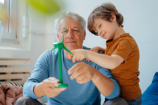 Smiling grandfather and grandson analyzing wind turbine model at home