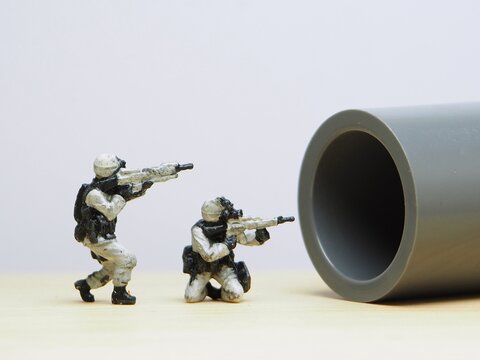 Mini toy of action figure at table with blurred background. Miniature photography concept design. Minifigure of army character with weapon at battlefield.