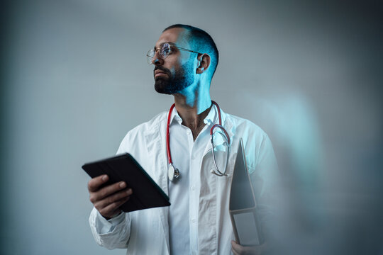 Doctor holding tablet PC and file folder in front of wall