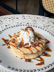Fluffy pancakes topped with vanilla ice cream, chocolate flakes, and caramel drizzle, served on a ceramic plate—perfect for breakfast or dessert inspiration.