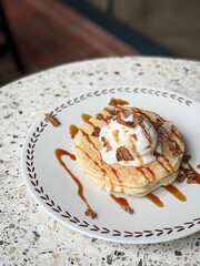 Fluffy pancakes topped with vanilla ice cream, chocolate flakes, and caramel drizzle, served on a ceramic plate—perfect for breakfast or dessert inspiration.