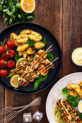 Greek style chicken skewers souvlaki with roasted potatoes and cherry tomatoes on wooden background	