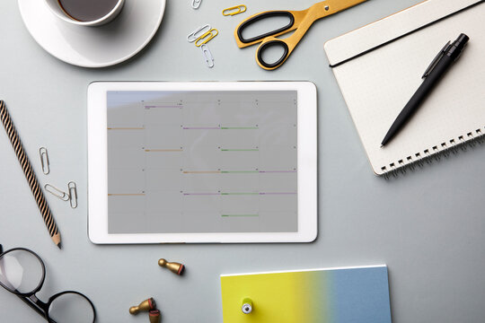 Overhead view of a desk with a tablet displaying a calendar and various office supplies