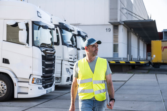 Confident mature foreperson wearing reflective workwear walking with tablet PC outside warehouse