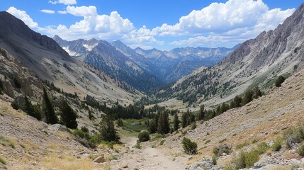 Panoramic view of a mountain valley, showing a dirt path leading down towards a lush green valley floor nestled between steep, rocky mountains under a partly cloudy sky