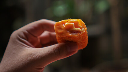 Jakarta, Indonesia 30 June 2025 : Hand holding a fried cheese roll with gooey cheese dripping....