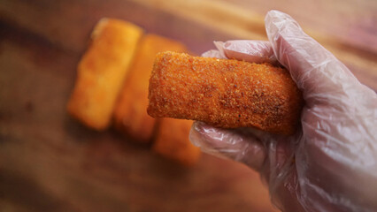 Jakarta, Indonesia 30 June 2025 : Hand holding a fried cheese roll with gooey cheese dripping....