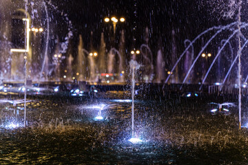 A close-up of the water surface and the spray of the city fountains, which are illuminated by colorful lights at night.