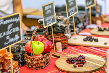 Colorful apples in wicker basket on market stall beside handmade fruit marmalade. Concept of fresh produce and artisanal natural fruit candy, marmalade presentation