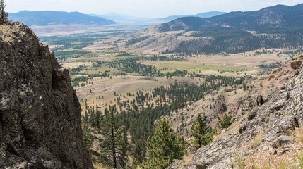 Fototapeta premium Panoramic view of a valley nestled between rocky mountains, showcasing diverse terrain, vegetation, and distant mountain ranges under a clear sky