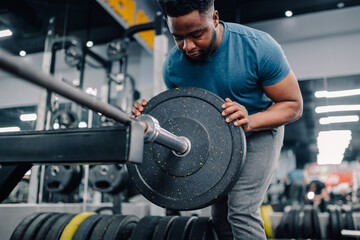 Determined bodybuilder adding weights to barbell in gym