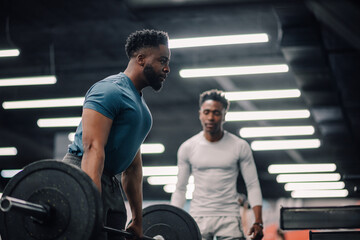 Determined bodybuilder lifting weights while personal trainer watching him in the gym