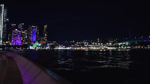 Sydney, Australia - June 11, 2025: HD Video - Colourful Sydney City Waterfront by night -Pan view from East Circular Quay to Harbour Bridge during Vivid Sydney Lights Festival. 