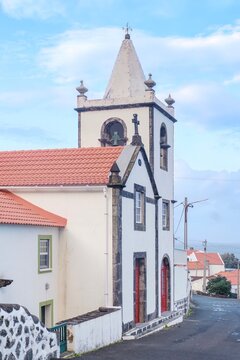 Traditional Portuguese Church With Bell Tower in Sao Jorge Azores Village. White architecture, terracotta roof tiles, volcanic stone trim, Atlantic islands