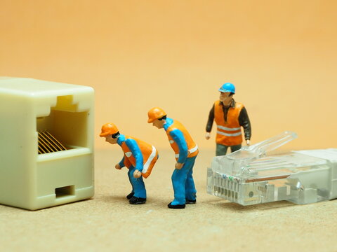 Mini toy of action figure at outdoor with blurred background. Miniature photography concept design. IT engineer with UTP cable. - Powered by Adobe