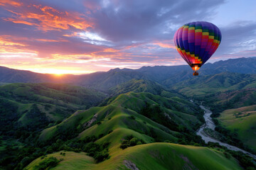 Fototapeta premium Colorful hot air balloon floats over lush green hills at sunrise in mountainous landscape