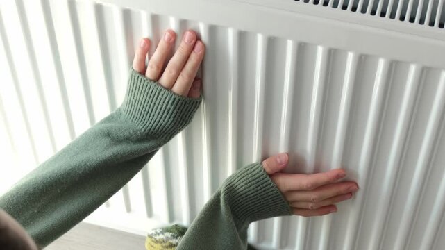 Female person puts feet in grey woolen socks on room central heating radiator. Owner gets cold and tries to warm up feet and hands in uncomfortable apartment in winter. Utility services problems