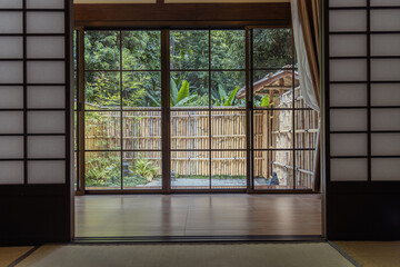 Traditional Japanese room with sliding doors opens to peaceful garden with bamboo fence and lush green plants creating calm and serene atmosphere perfect for relaxation and meditation