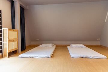 Minimalist bedroom with two floor mattresses and pillows on wooden floor under slanted ceiling...