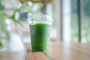 Green tea drink with foam in plastic cup on wooden table with blurred background creating calm mood and t cell cancer research concept