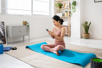 Happy young fitness asian woman using cell phone app after workout at home. Technology and healthy lifestyle concept.