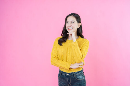 In the heart of the shoot, an Asian female model is posing and taking photos in a studio with a pink background, perfectly blending style, fashion, and advertising elements. - Powered by Adobe