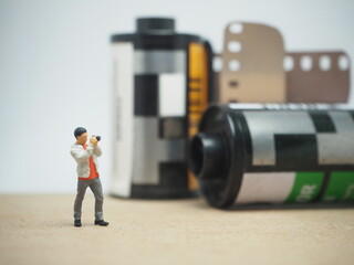 Mini toy of action figure and 35 mm roll film at outdoor with blurred background. Analog photography concept design. Minifigure of photographer with pocket camera.