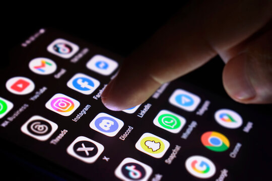 The phone screen lights up the various social media applications. The index finger touches the Discord application, 30 June 2025, Lopburi Province, Thailand.