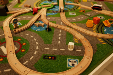 Wooden toy railway set placed on a colorful play mat with roads, signs and toy accessories for...
