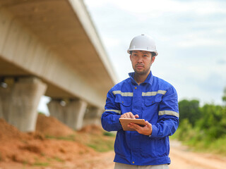 Caucasian young beautiful woman architect or builder in the hardhat standing at the roof of the building site and using tablet device, tapping and scrolling.