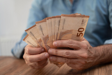 Male financial manager carefully counts euro banknotes preparing money for paying monthly salary to...