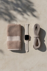 lat lay of unbranded smartwatch, resistance band, and towel on matte plaster surface, neutral colors