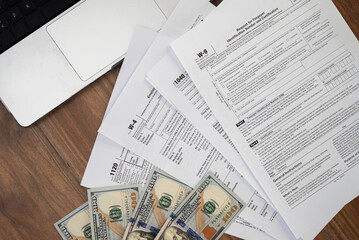 Different forms on table demonstrate preparation process for corporate tax deadlines before filling tax blanks near laptop and dollar bills at wooden workplace