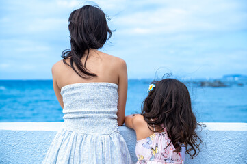 Smiling mother and daughter looking at each other in front of the ocean on a windy summer day