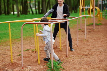 father and son navigate playground obstacle course in outdoor park. child runs through vibrant...