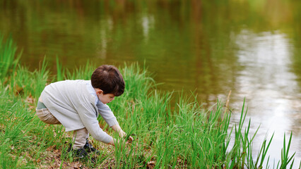 child exploring nature near pond in early spring, bending over to observe insects in green grass....